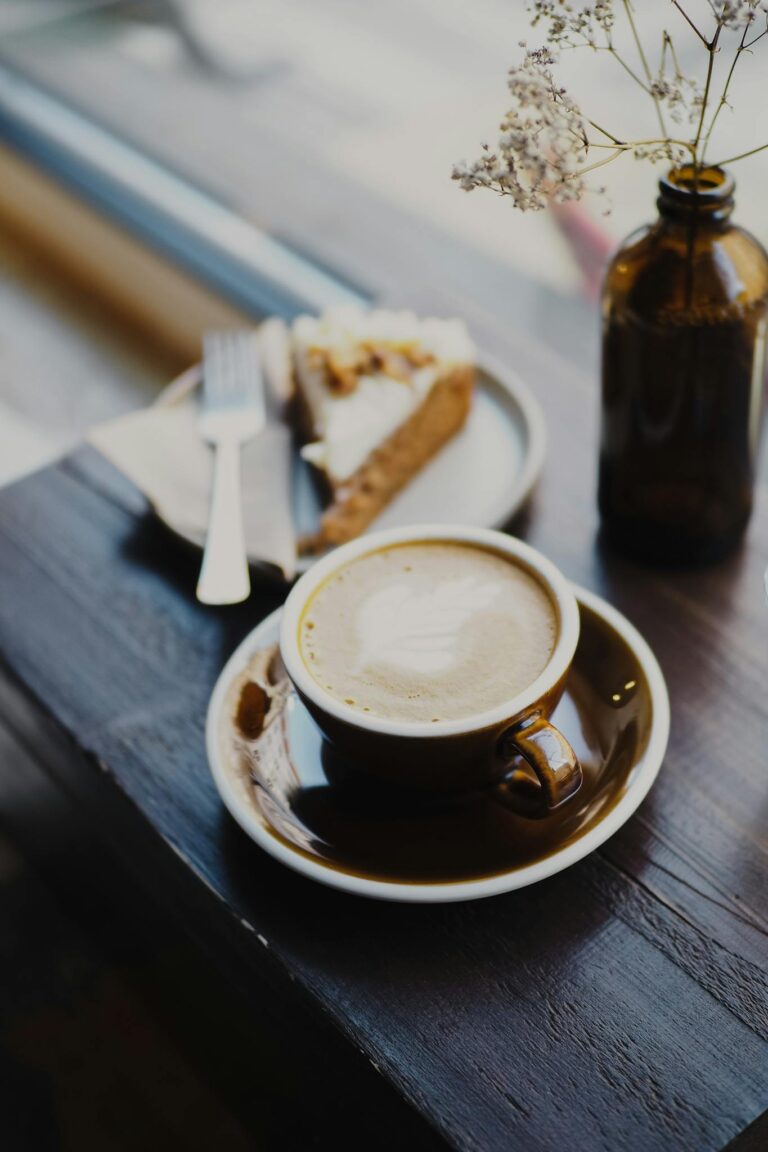 Close-up of a coffee cup and dessert on a wooden table in a cozy café setting.