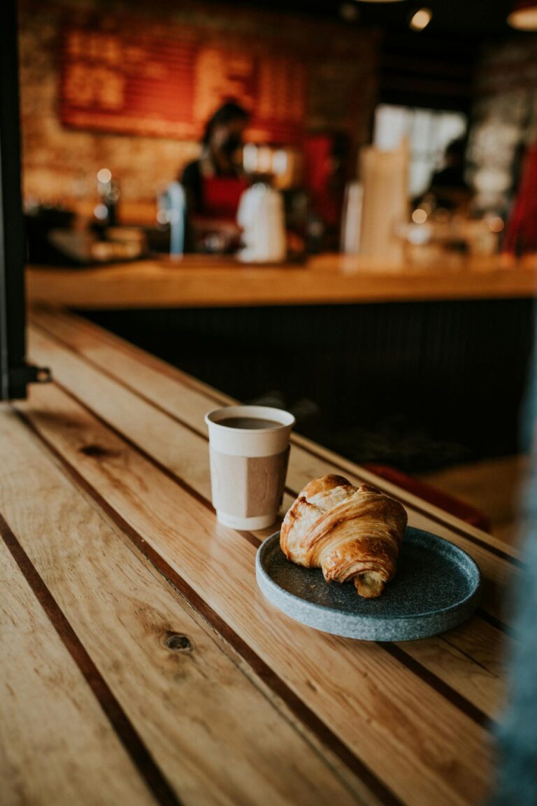 Warm café scene featuring a croissant and cup of coffee on a wooden table, perfect for breakfast imagery.