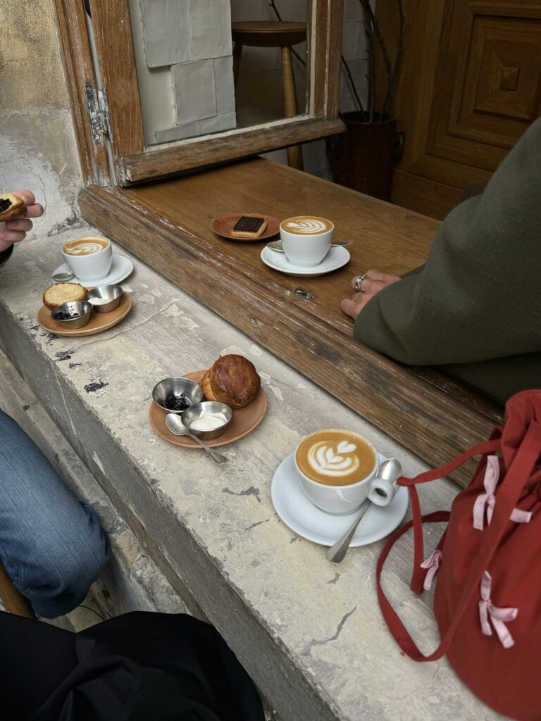 Warm coffee shop scene featuring lattes and pastries on a rustic stone ledge.